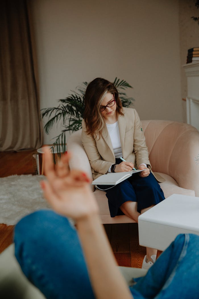 A therapist in a modern office takes notes while listening to a client.